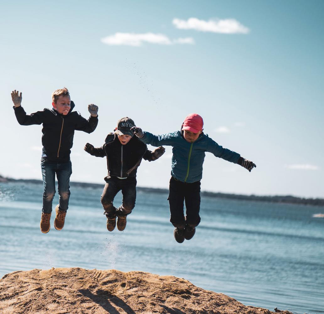 tre barn som hoppar med havet i bakgrunden