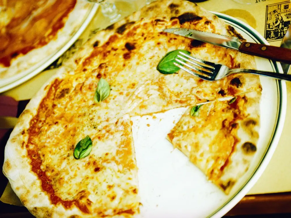 En ost-pizza som saknar en slice och som har några salladsblad