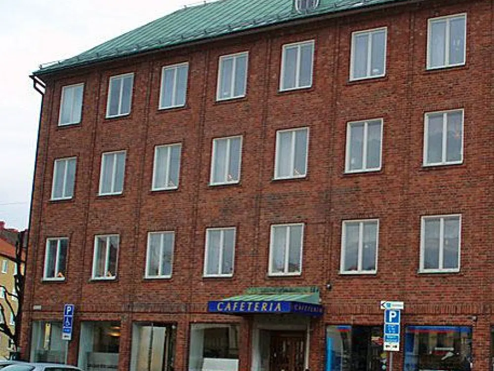 Brunbyggnad med många fönster och bilar som står utanför på parkeringen