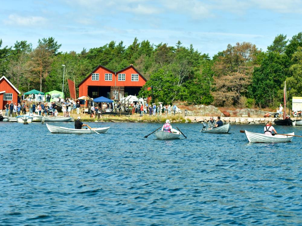 Bild tagen från havet in mot hästholmen, på röda byggnader och mycket folk både i vattnet i båtar samt uppe på land
